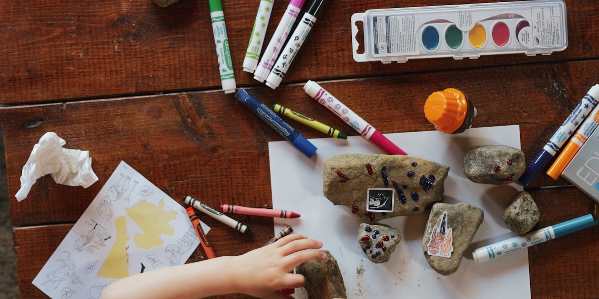 Mesa de taller con materiales de arte: ceras, acuarelas y piedras pintadas por los niños